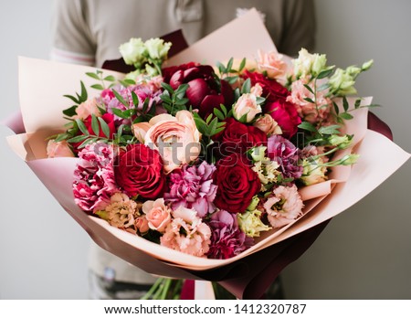 Very nice young woman holding big and beautiful bouquet of fresh eustoma, roses, ranunculus, carnations, peony in cream, pink and burgundy colors, cropped photo, bouquet close up Royalty-Free Stock Photo #1412320787