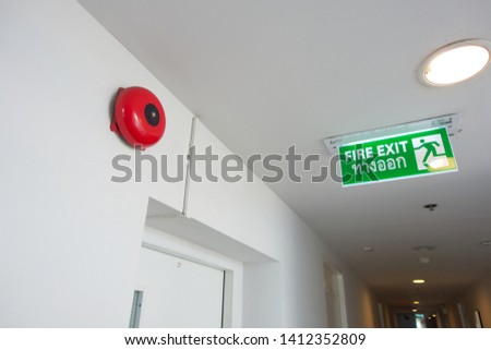 red fire alarm bell on white wall and fire exit sign