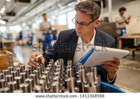 Factory engineer doing quality control inspection of manufactured steel cylinders in industrial building.  Royalty-Free Stock Photo #1412368988