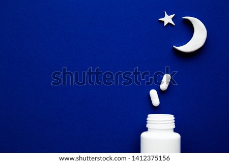 White bottle with pills and moon on dark blue background. Sleeplessness and healthcare concept. Copy space. Empty place for text or logo. Flat lay.