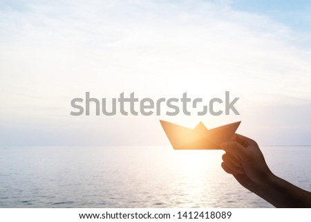 Silhouette hand holding boat sign at seascape sunset sky.  concept of freedom and believe.