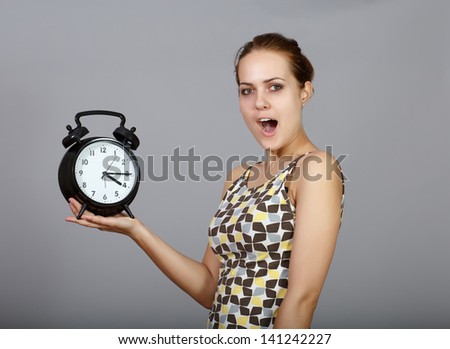Surprised woman with alarm clock in the studio at gray background