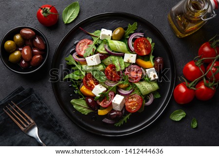 Fresh greek salad with tomato, cucumber, bel pepper , olives and feta cheese on black plate, top view, dark background Royalty-Free Stock Photo #1412444636