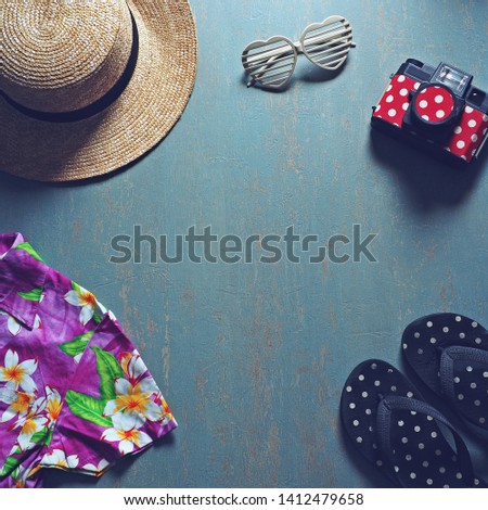 Summer holiday preparation checklist - Straw boater hat with black ribbon, plastic heart shaped glasses, toy camera, flip flop sandal, colorful Hawaiian shirt on weathered blue background /square crop