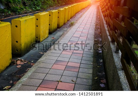 Yellow barriers placed along the road between the walkway path for safety on dangerous curves or risk zone of street with sunlight background.