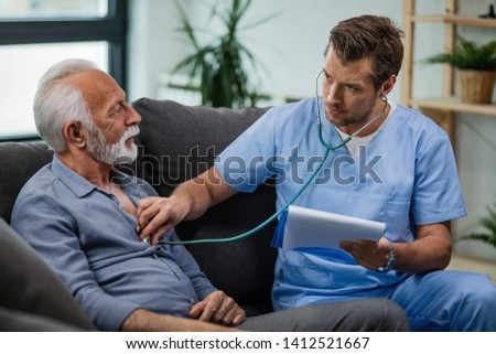 Healthcare worker using stethoscope and listening to heartbeat of his mature patient during a home visit.  Royalty-Free Stock Photo #1412521667