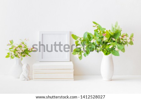 Home interior with decor elements. White frame, branches with green leaves in a vase, interior decoration