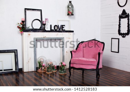 Vintage velor armchair, in a bright room and an artificial fireplace. Interior attic with wooden white walls. Picture frames on the wall. The space where you can put a person. Gothic style room. 