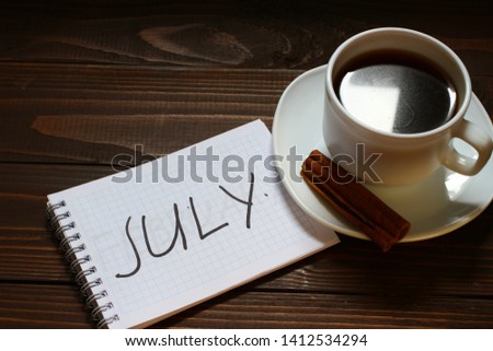 July inscription and word in a notebook near a cup of coffee