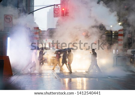 Undefined people with umbrellas are crossing the 42nd street in Manhattan. Steam coming out from from the manholes in the background. Manhattan, New York City, Usa.