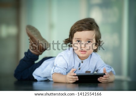 Cute 3 years old boy lying down on the table holding smart phone watch cartoon.  toddler addicted to phone. 