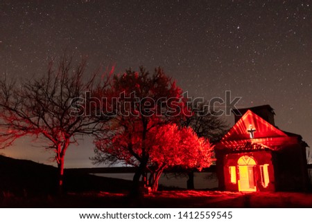 Abandoned church with red light inside and blooming trees nearby nightscape
