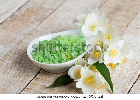 Sea salt in bowl with flower of jasmine on wooden background. Selective focus.