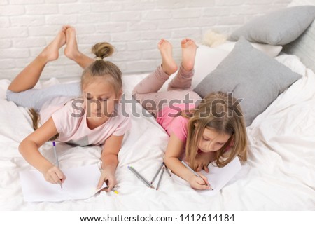 two cute children girls playing in the bedroom. kids drawing pictures while lying on bed. pajama party and friendship.