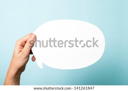 Hand holding a white blank speech bubble on blue background.