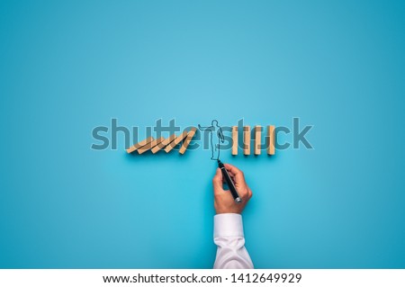 Handdrawn shape of a businessman stopping falling dominos. Over blue background.