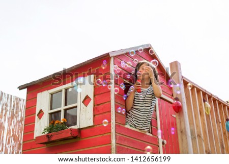 Boy blowing bubbles from a wooden playhouse Royalty-Free Stock Photo #1412656199