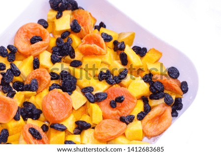 Pumpkin dessert with dried fruits in a ceramic form before roasting a closeup on a white background it is horizontally.Pumpkin pieces,raisin,dried apricots at a stage of preparation of a sweet dessert