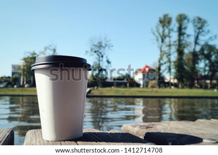 A cup of coffee stands on a wooden pier near the lake.

