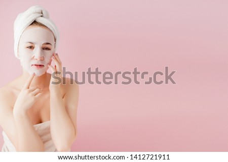 Beautiful young woman is applying a cosmetic tissue mask on a face on a pink background. Healthcare and beauty treatment and technology concept.