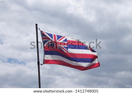 Flag of Hawaii on pole with clouds in the background