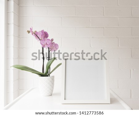 White blank square frame on table with purple striped phalaenopsis order against painted brick wall (selective focus)