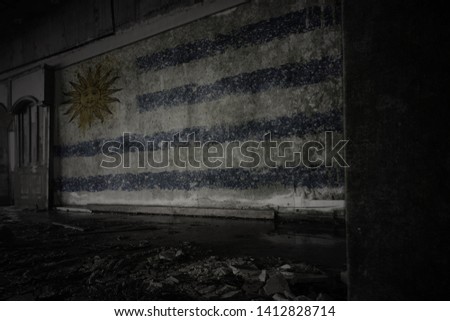 painted flag of uruguay on the dirty old wall in an abandoned ruined house. concept