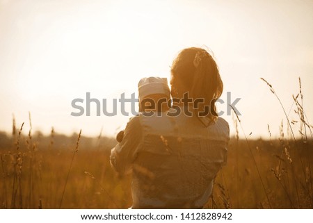 Happy child and his mom have fun outdoors in a field flooded with . Mom holds the child in her arms, and the child hugs and kisses the mother