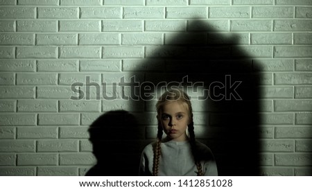 Orphan female kid looking at camera, needs family, house shadow on background