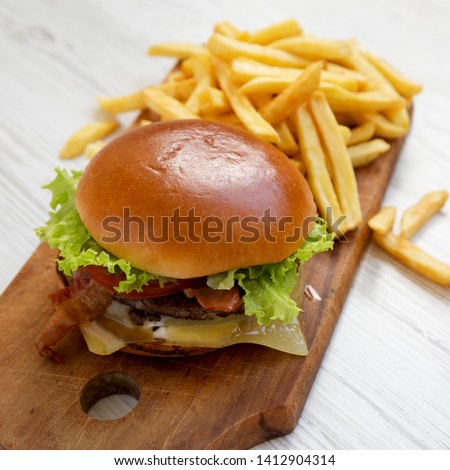 Hamburger with lettuce, cheese and bacon on a rustic wooden board on a white wooden table, side view. Close-up.
