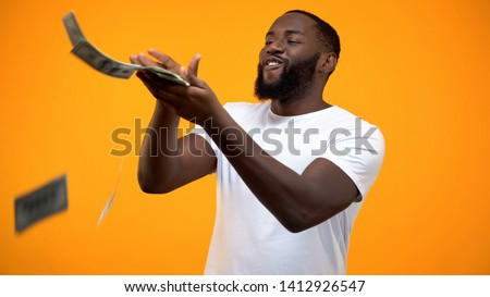 Happy African-American man throwing dollars banknotes, wasting money, concept Royalty-Free Stock Photo #1412926547