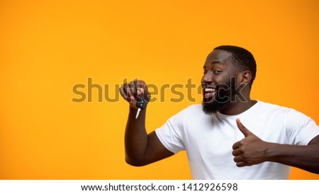 Excited Afro-American man holding car key and showing thumbs up, purchase