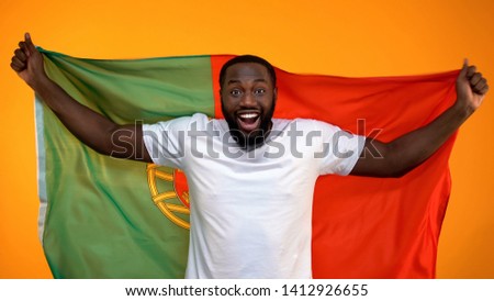 Amazed Afro-American sport fan holding Portuguese flag, cheering for victory