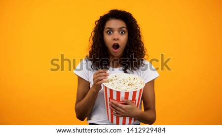 Excited African-American woman eating popcorn and watching interesting movie