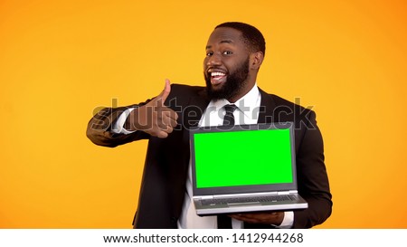 Happy smiling afro-american male showing prekeyed laptop and thumbs-up gesture