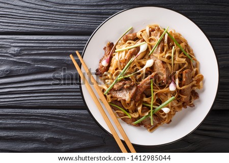 Beef Chow Fun a staple Cantonese dish, made from stir-frying beef, wide rice noodles and vegetables closeup on the plate on the wooden table. Horizontal top view from above
 Royalty-Free Stock Photo #1412985044
