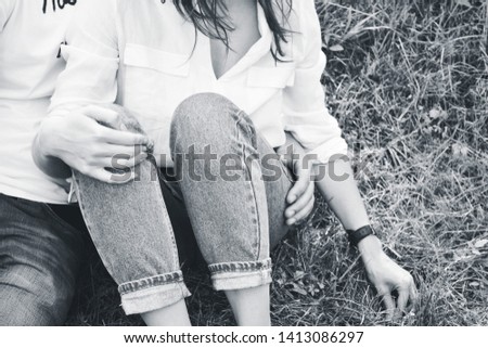 black and white photo of a young couple sitting on the grass facing the viewer; but faces are invisible; there are legs,hands,elbows