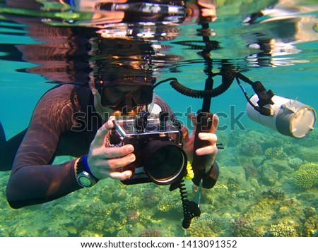 Photographer snorkeling with underwater camera on the coral reef. Shallow tropical sea and tourist with camera. Underwater photography from snorkeling. Corals in the ocean, aquatic life.