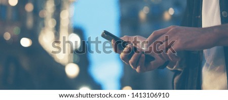 Closeup image of male hands with smartphone at night on city street, searching internet or social networks, hipster man typing an sms message on chat, bokeh lights