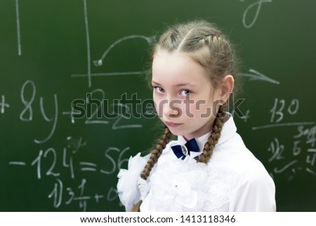 Schoolgirl teenager sad at the school blackboard. Girl student 10-12 years of age in sadness sad because a poor assessment of knowledge.