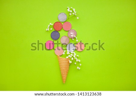 The concept of beauty and fashion. Multicolored round eyeshadow with gypsophila in a cone for ice cream on a green background