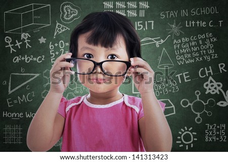 Cute asian girl holding glasses in classroom