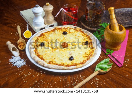 Bio pizza 4 cheeses with black olives and tomatoes sauce. Presented with spicy oil and several decorative elements. Served on a round wooden table.