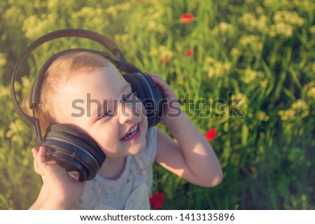 Happy smaill girl listen to the music in the earphones. Child walking in the field of poppy flowers