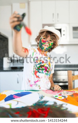 Happy child painting with colorful paintings in the kitchen of his house