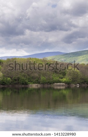 Beautiful, sunlit, vivid green trees in a forest during early spring around Sukovo lake reflecting the trees and cloudy sky in a calm water