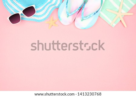 Beach accessories on a pink background. Summer vacation concept top border with copy space. Sunglasses, sea shells, towel, flip flops and blue striped hat. 