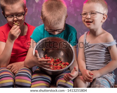 Funny little boys blond eating ripe strawberries from large pot. Kids helped to harvest with mom in garden and now enjoys. Children eat healthy organic foods, fresh berries