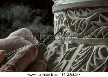 Closeup dusty hands of unrecognizable artisan using electric chisel to carve floral ornament on plaster surface in studio