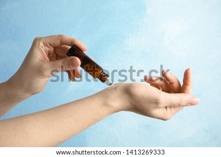 Woman applying essential oil on her wrist against color background, closeup Royalty-Free Stock Photo #1413269333
